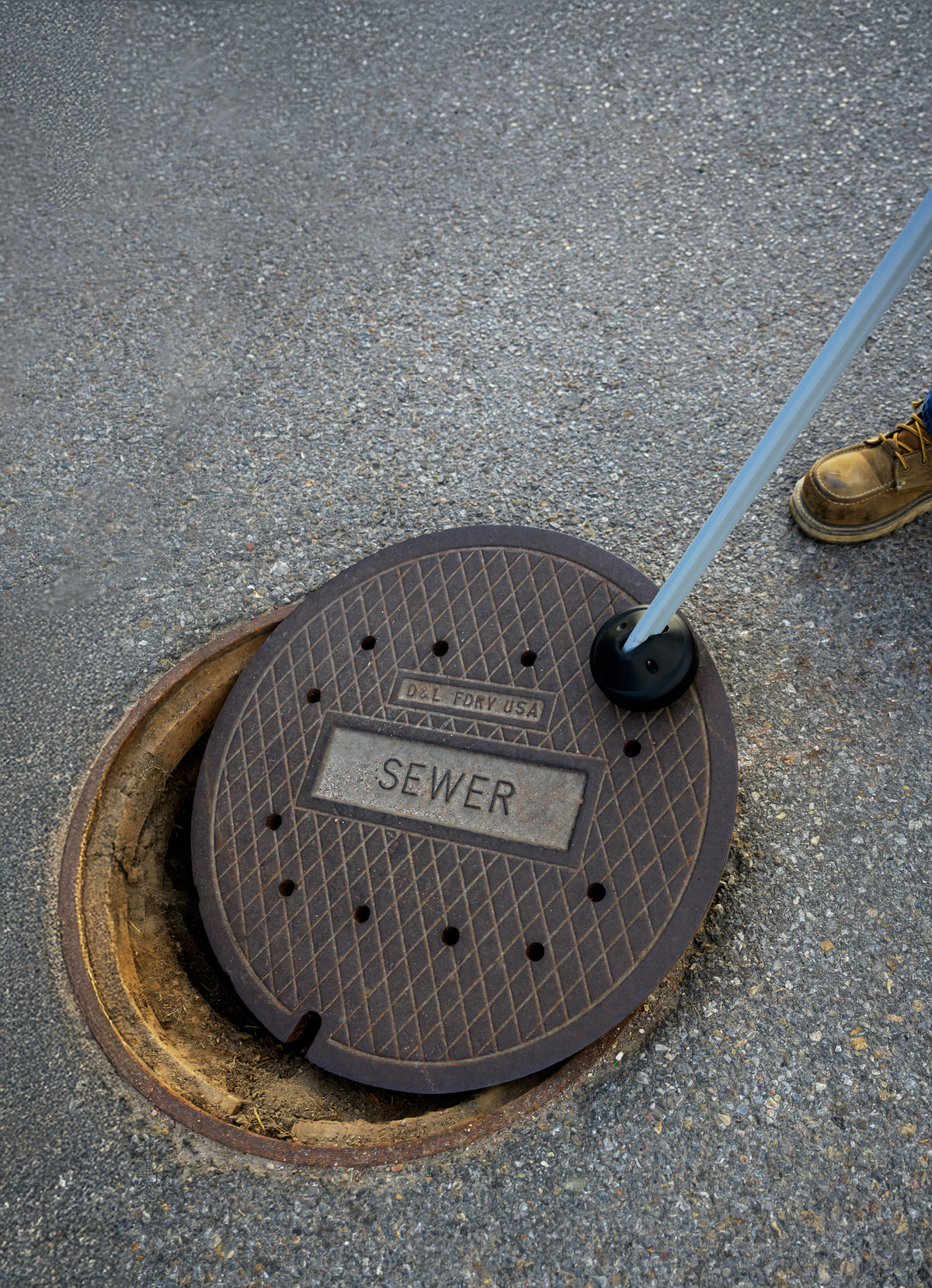 Top-down aerial view of EZLyft removing sewer lid — open manhole visible