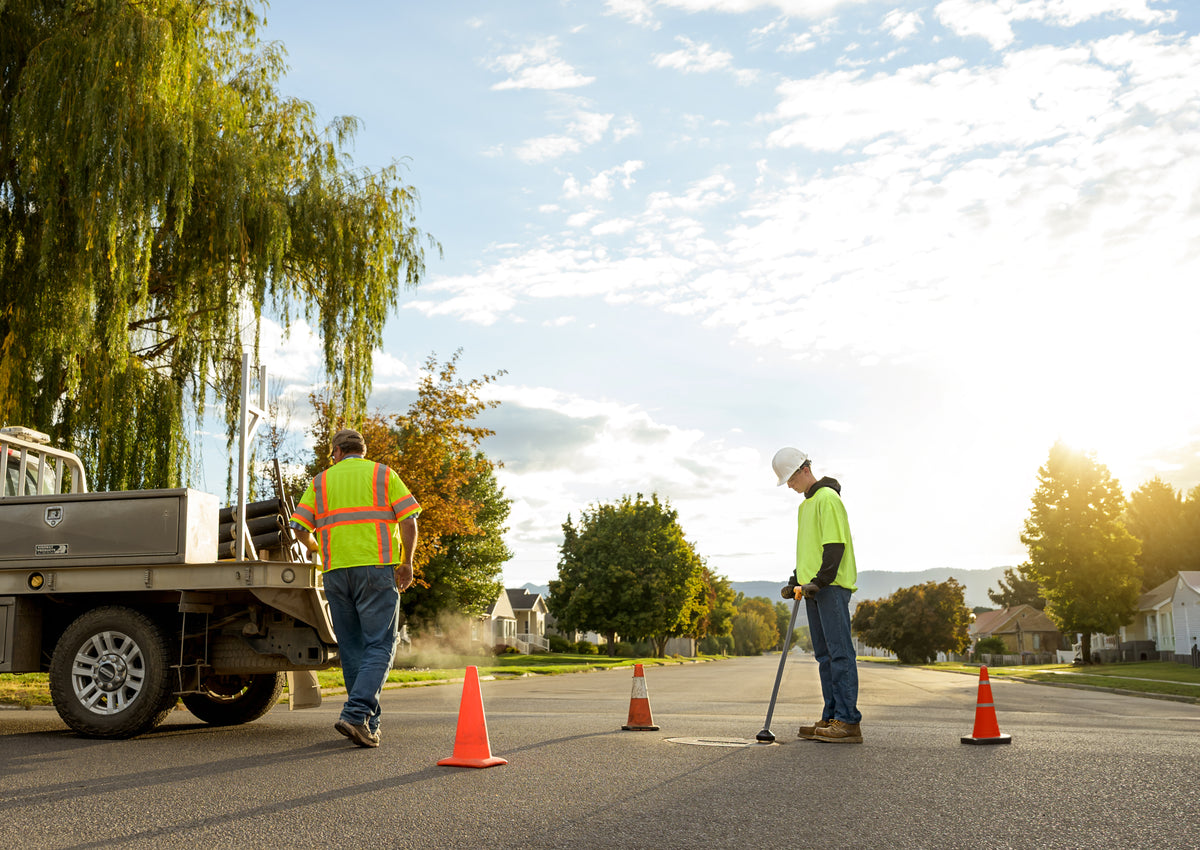 Utility worker lifting heavy sewer manhole cover with EZLyft magnetic tool — field use golden hour